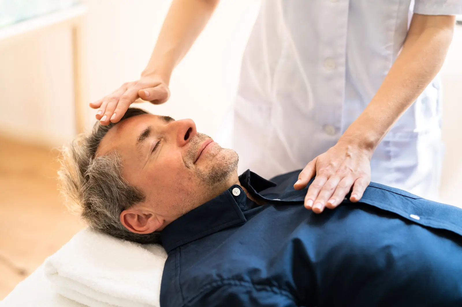 Reiki practitioner working with a fully clothed male client lying on a treatment table